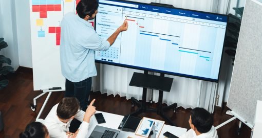 Project manager communicate and collaborate with team using project management software display on monitor, tracking progress of project task and making schedule plan at meeting table. Prudent
